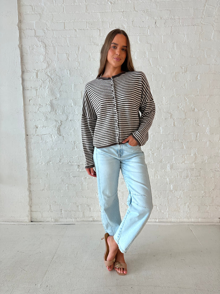 Woman wearing brown and cream striped knit cardigan with light wash barrel jeans. 