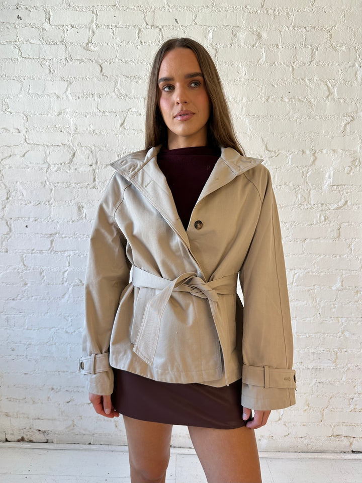 Woman wearing khaki colored jacket with belted waist, oversized collar, and plaid inside. 
