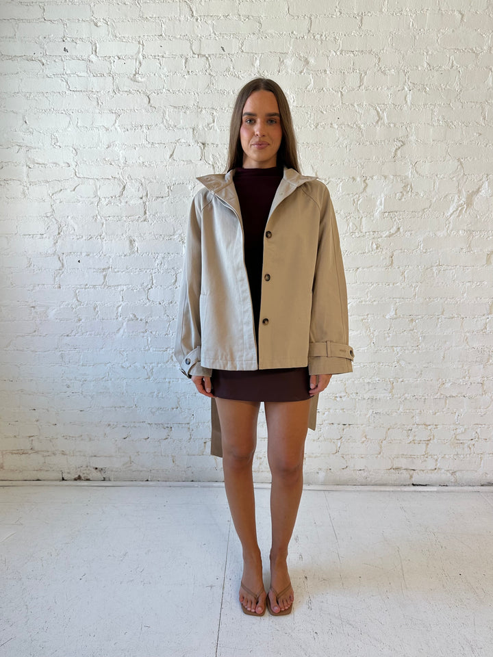 Woman wearing khaki colored jacket with belted waist, oversized collar, and plaid inside. 