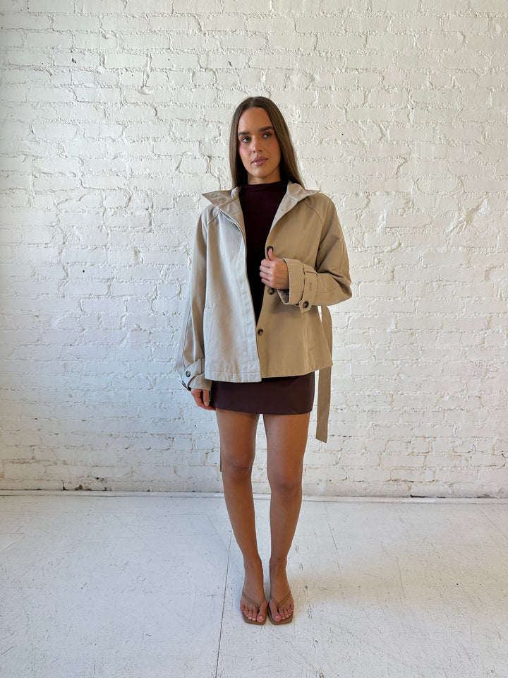 Woman wearing khaki colored jacket with belted waist, oversized collar, and plaid inside. 