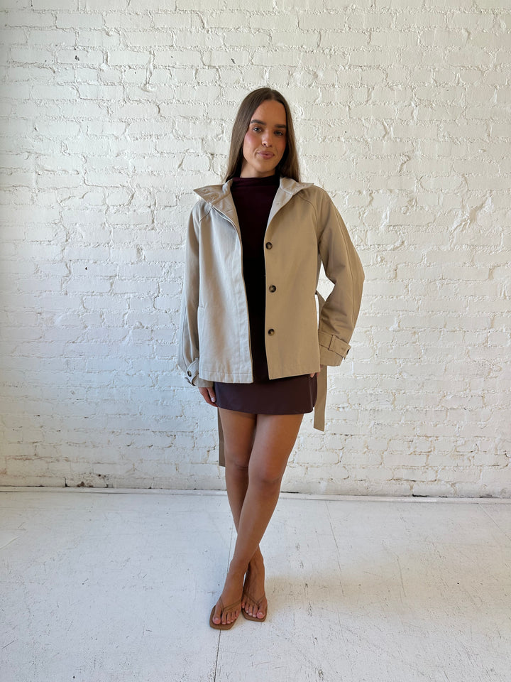 Woman wearing khaki colored jacket with belted waist, oversized collar, and plaid inside. 