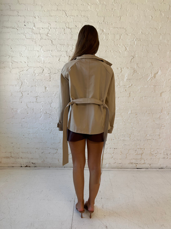 Woman wearing khaki colored jacket with belted waist, oversized collar, and plaid inside. 