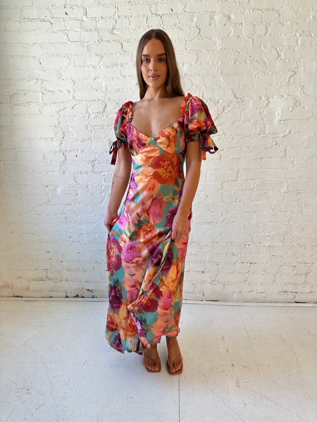 Woman wearing multicolor floral satin maxi dress with puff sleeves and tie detail.