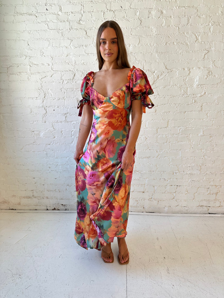 Woman wearing multicolor floral satin maxi dress with puff sleeves and tie detail.