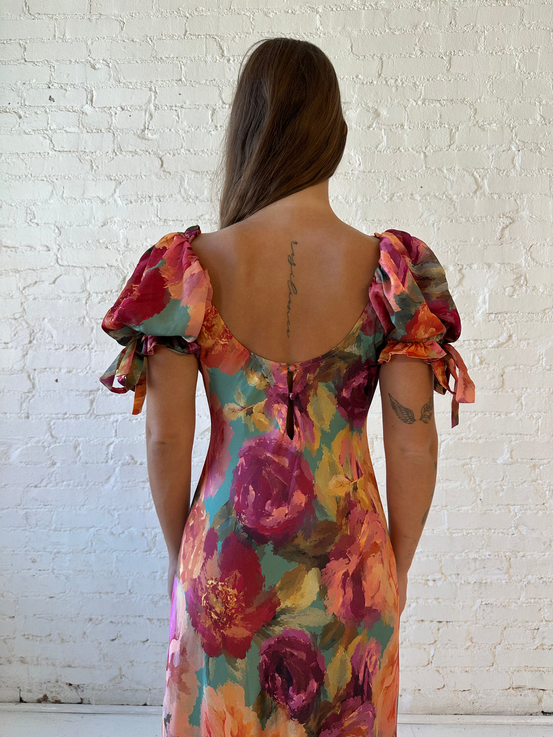 Woman wearing multicolor floral satin maxi dress with puff sleeves and tie detail.