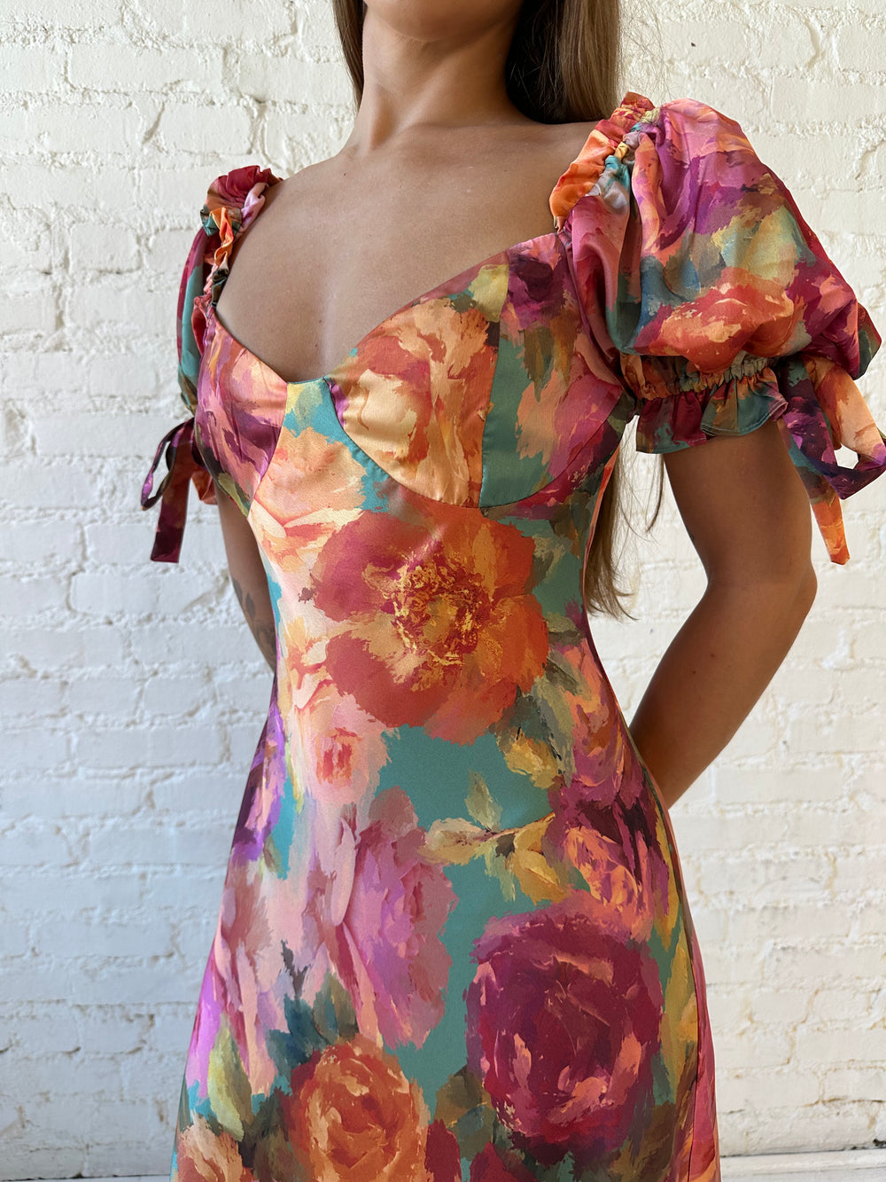 Woman wearing multicolor floral satin maxi dress with puff sleeves and tie detail.