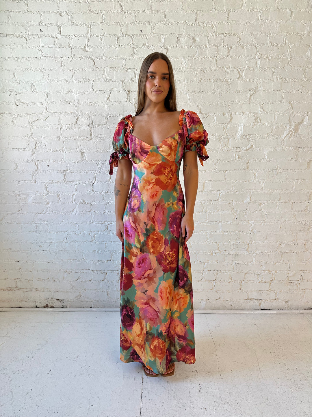 Woman wearing multicolor floral satin maxi dress with puff sleeves and tie detail.