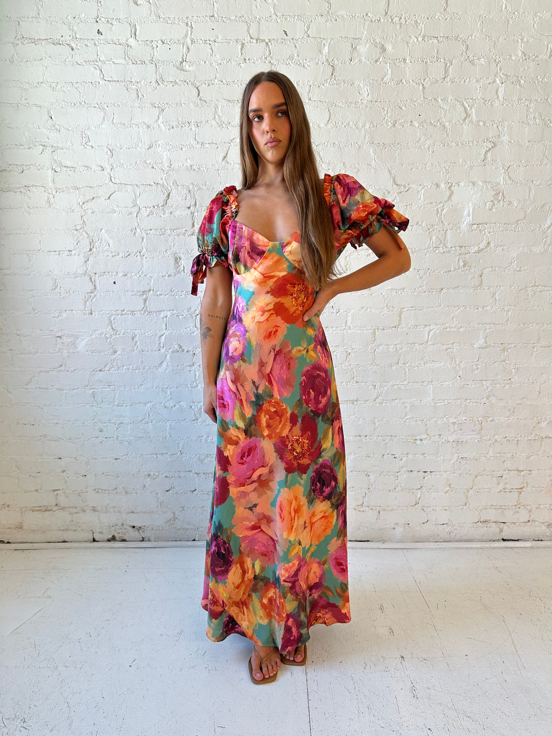Woman wearing multicolor floral satin maxi dress with puff sleeves and tie detail.