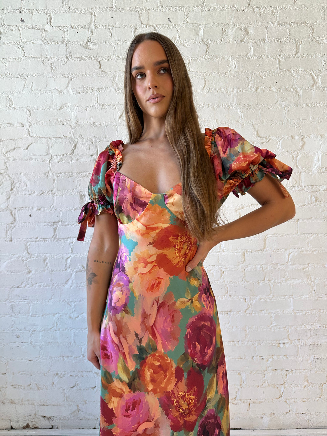 Woman wearing multicolor floral satin maxi dress with puff sleeves and tie detail.