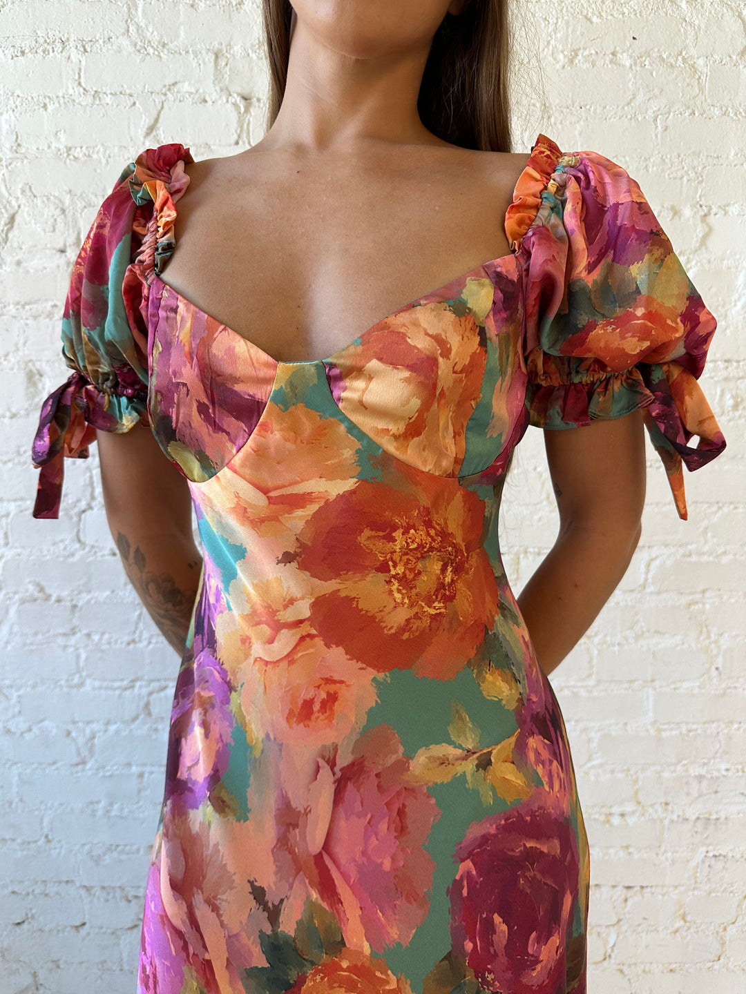 Woman wearing multicolor floral satin maxi dress with puff sleeves and tie detail.