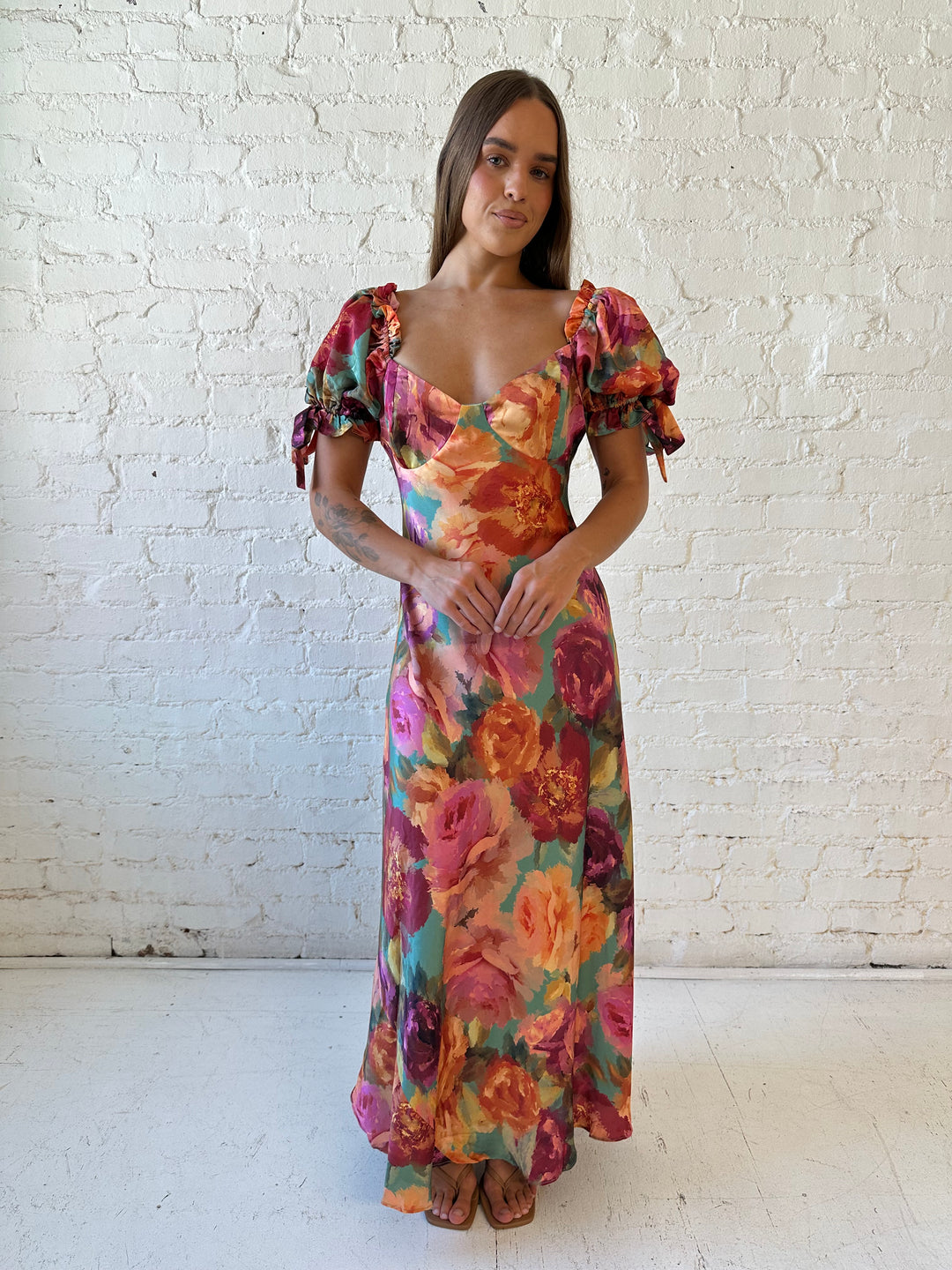 Woman wearing multicolor floral satin maxi dress with puff sleeves and tie detail.