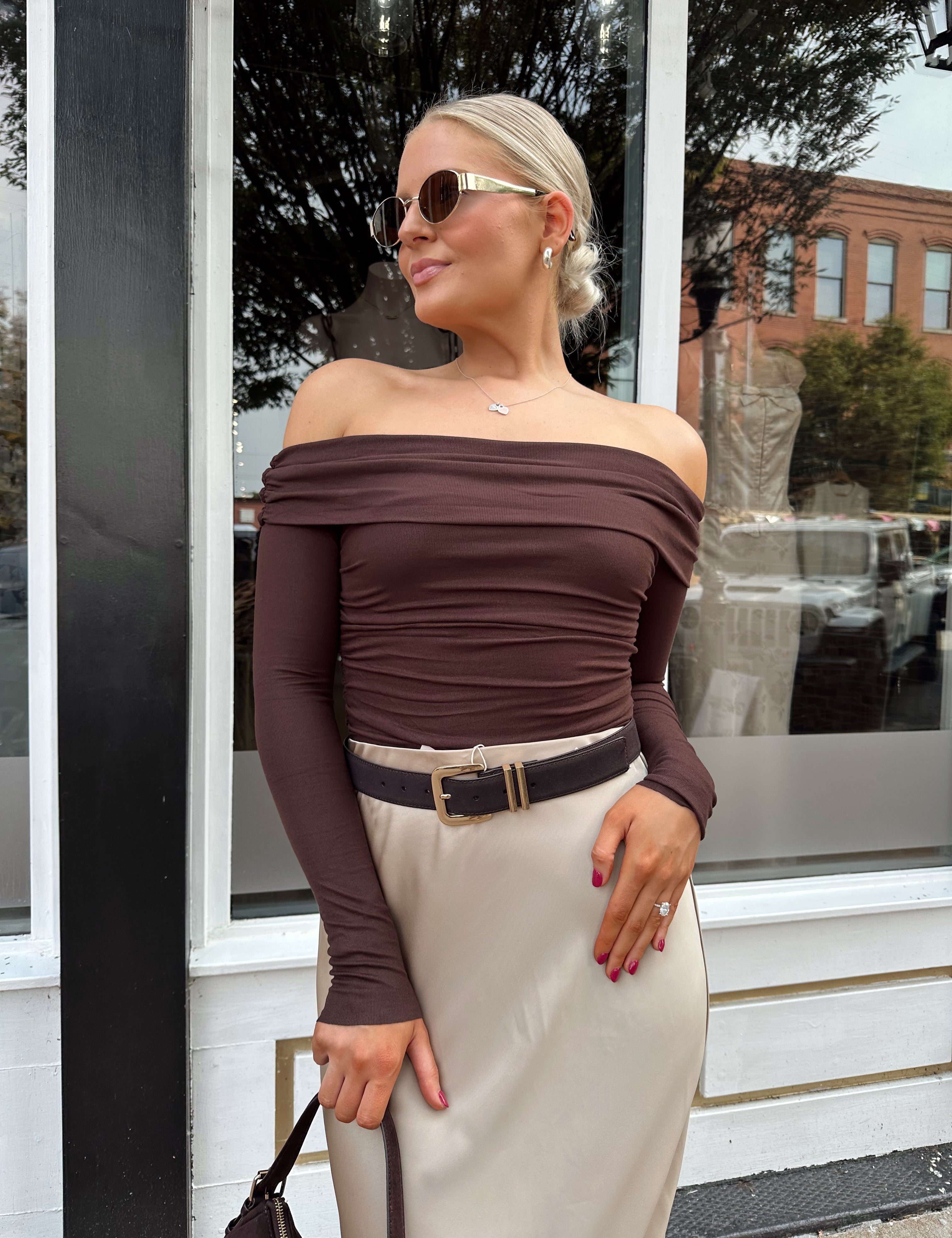 Woman wearing brown ribbed off the shoulder long sleeve bodysuit with champagne colored maxi skirt.