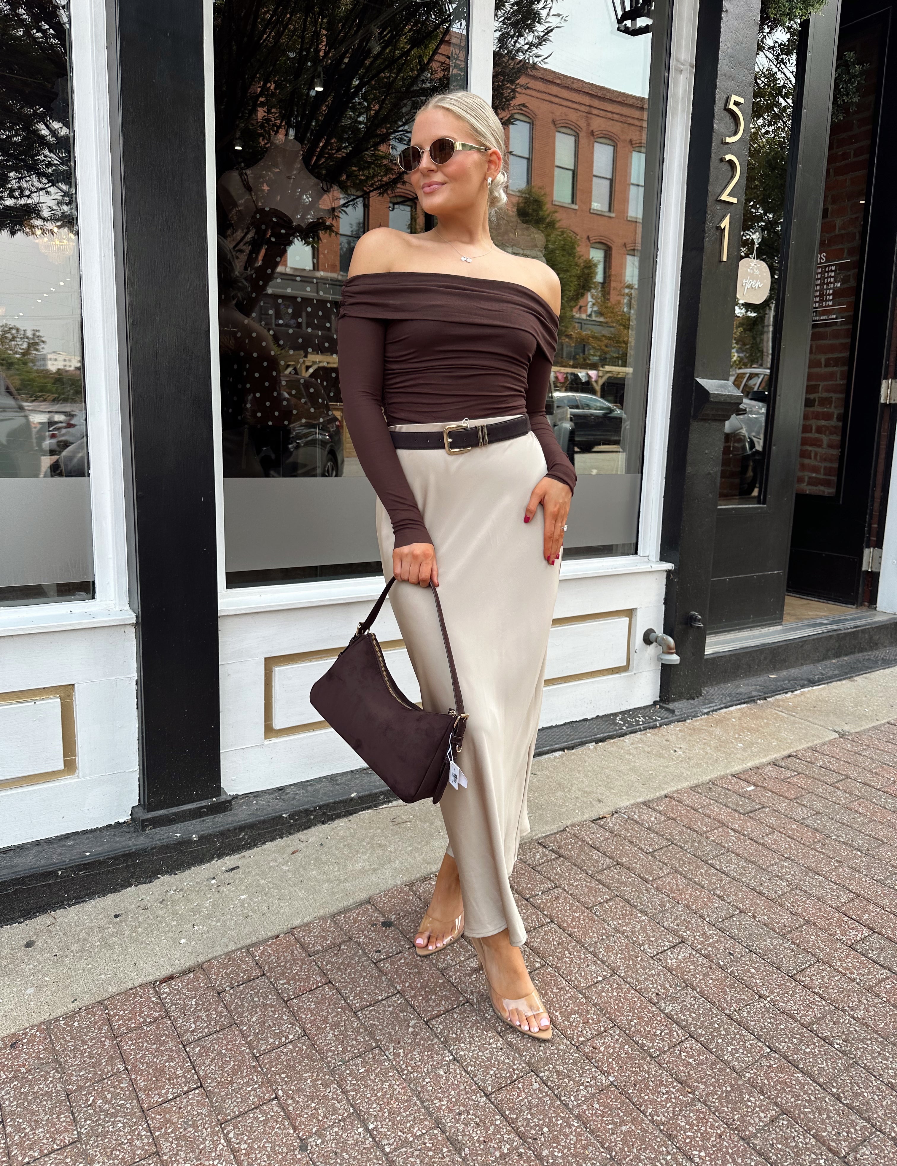 Woman wearing brown ribbed off the shoulder long sleeve bodysuit with champagne colored maxi skirt.