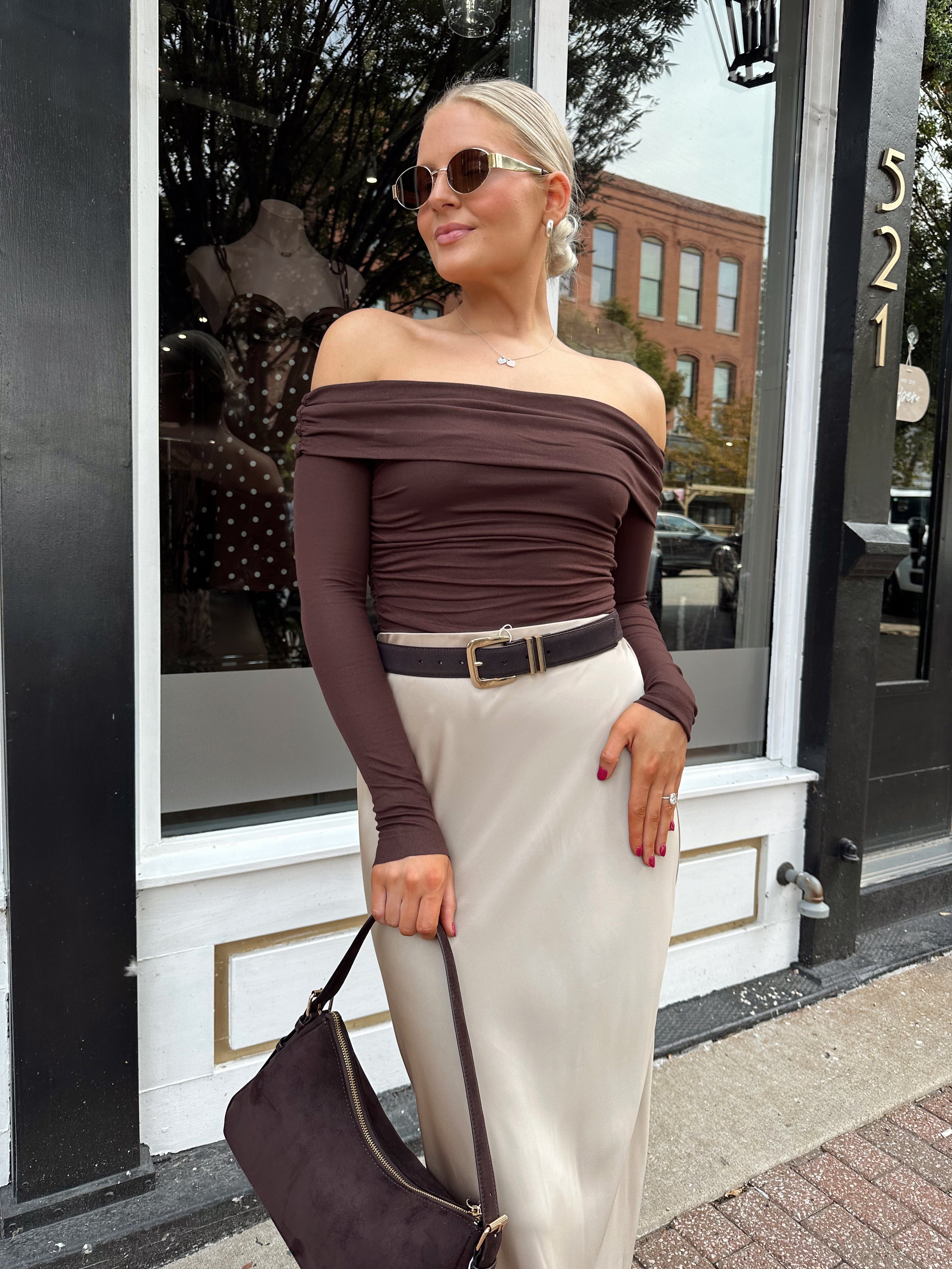 Woman wearing brown ribbed off the shoulder long sleeve bodysuit with champagne colored maxi skirt.