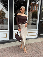 Woman wearing brown ribbed off the shoulder long sleeve bodysuit with champagne colored maxi skirt.