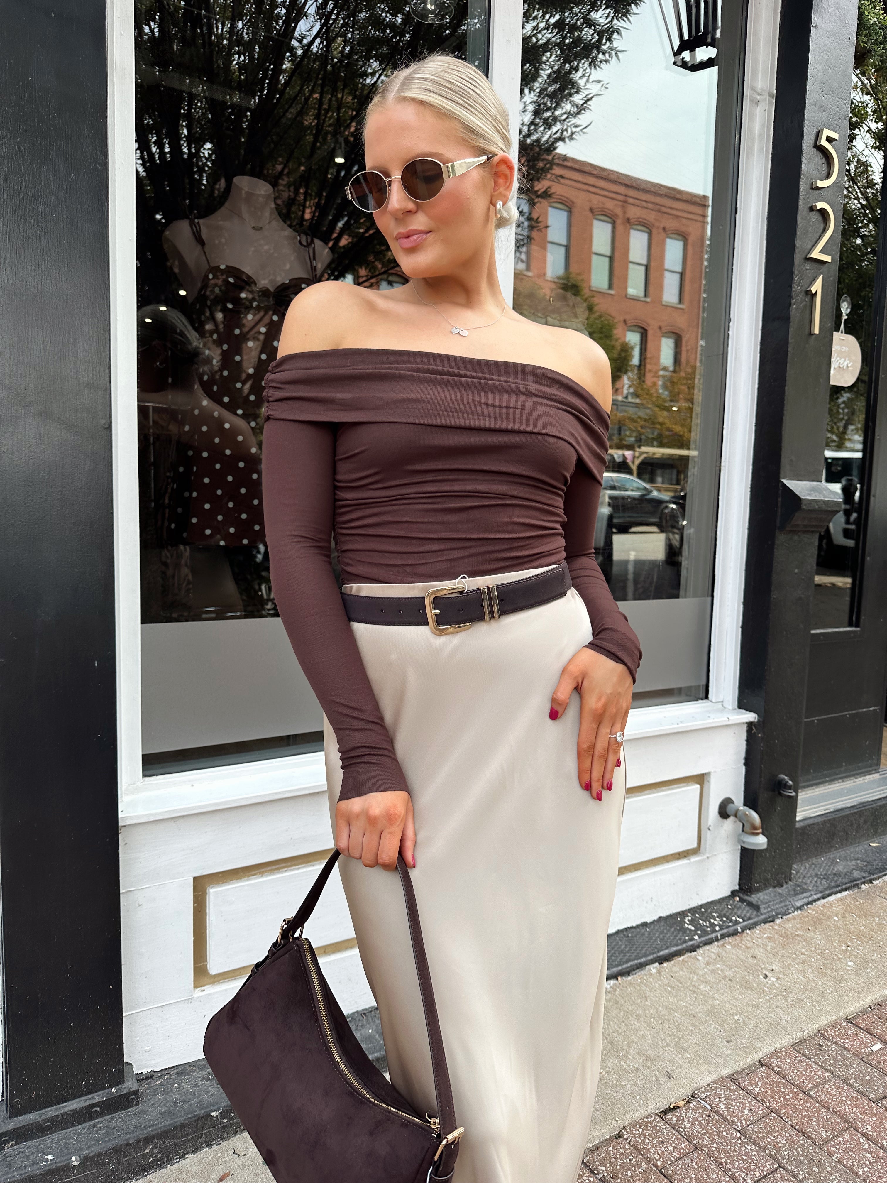 Woman wearing brown ribbed off the shoulder long sleeve bodysuit with champagne colored maxi skirt.