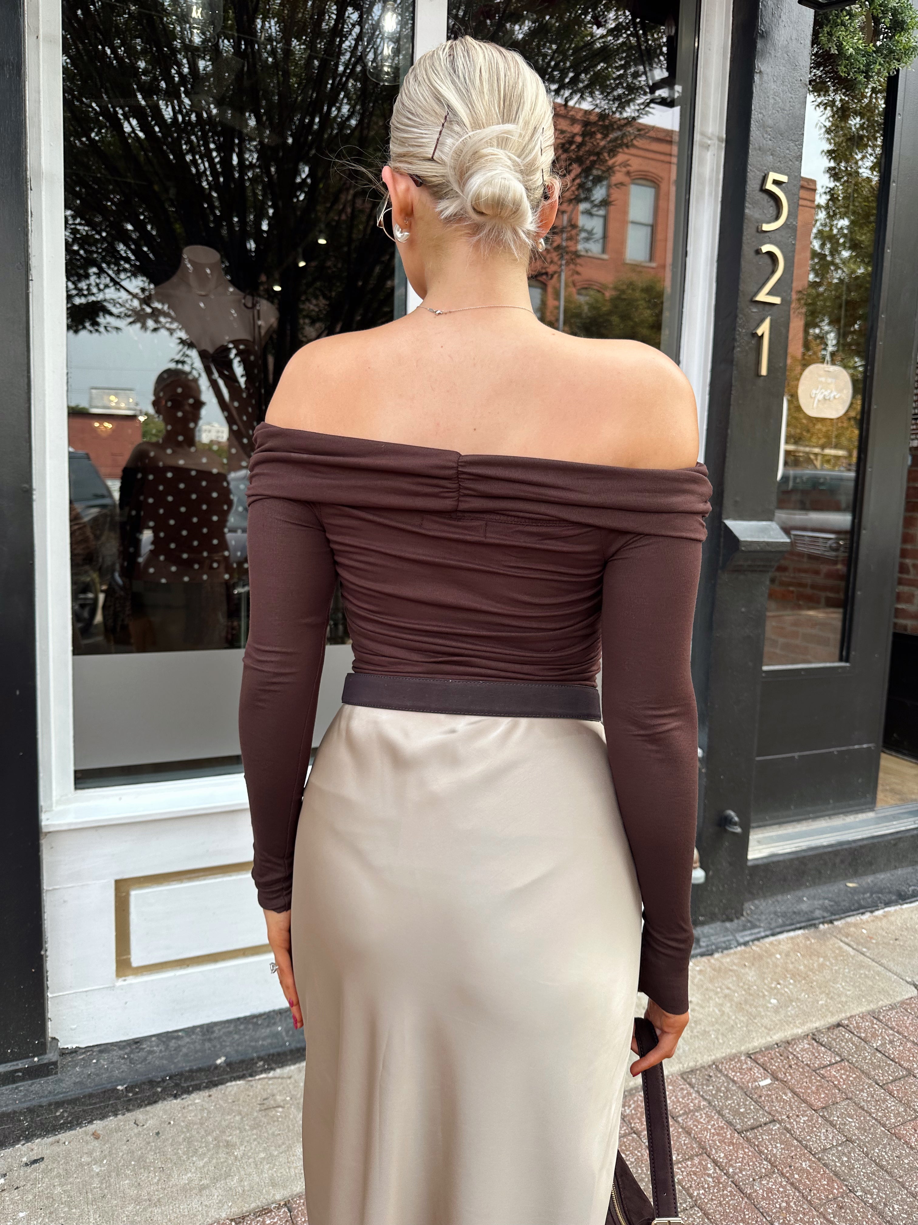 Woman wearing brown ribbed off the shoulder long sleeve bodysuit with champagne colored maxi skirt.