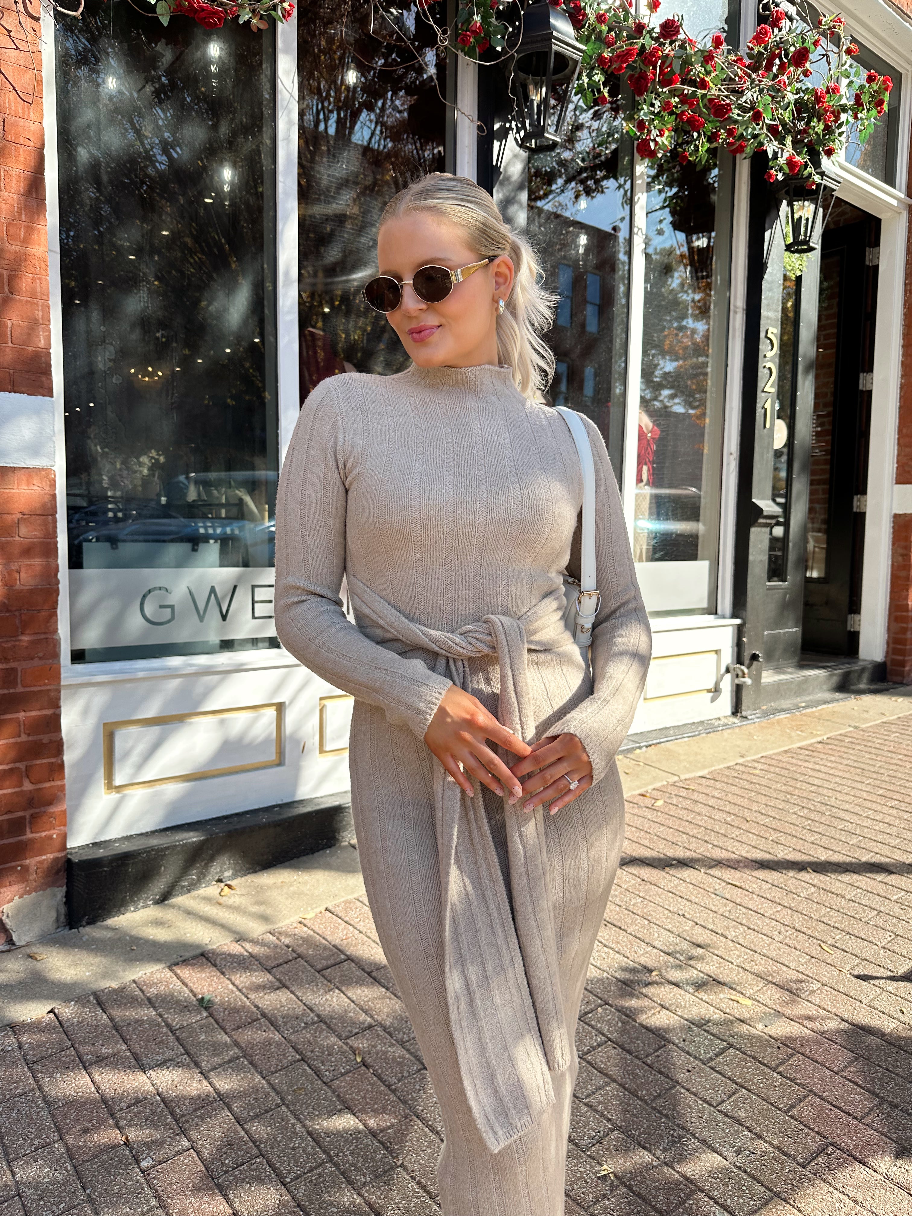 Woman wearing mocha long sleeve knit sweater dress with tie front detail. 