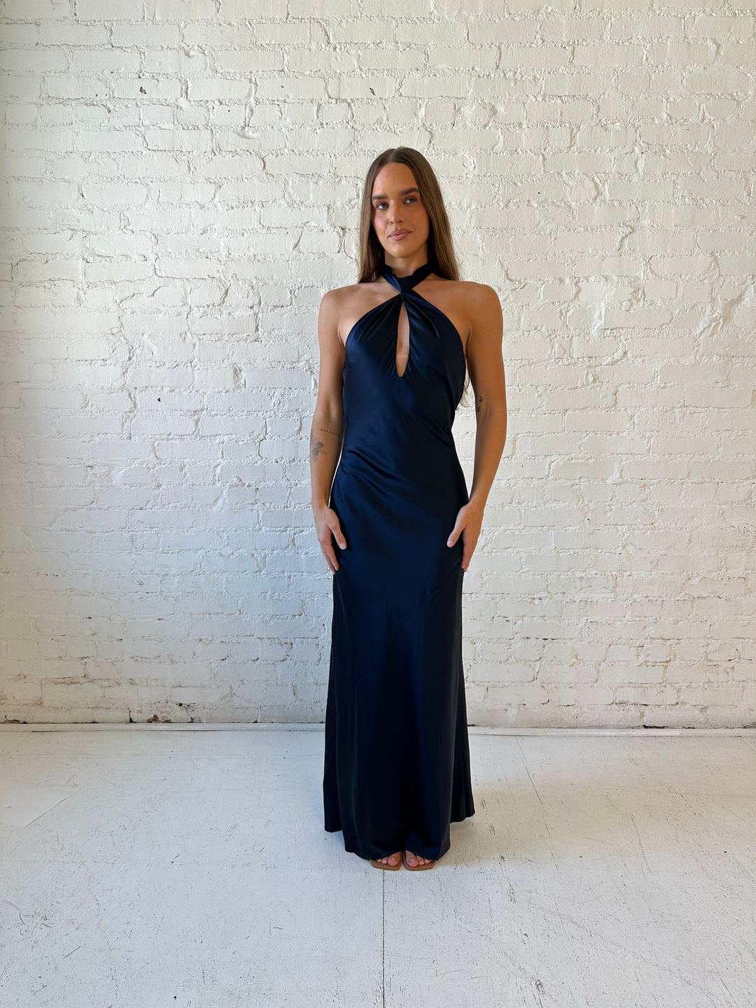 Woman wearing navy blue satin halter maxi dress with keyhole cutout, and open cowl back.