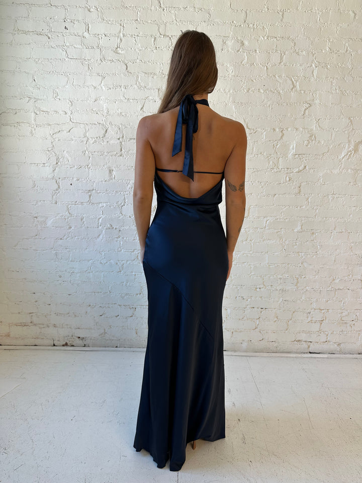 Woman wearing navy blue satin halter maxi dress with keyhole cutout, and open cowl back.