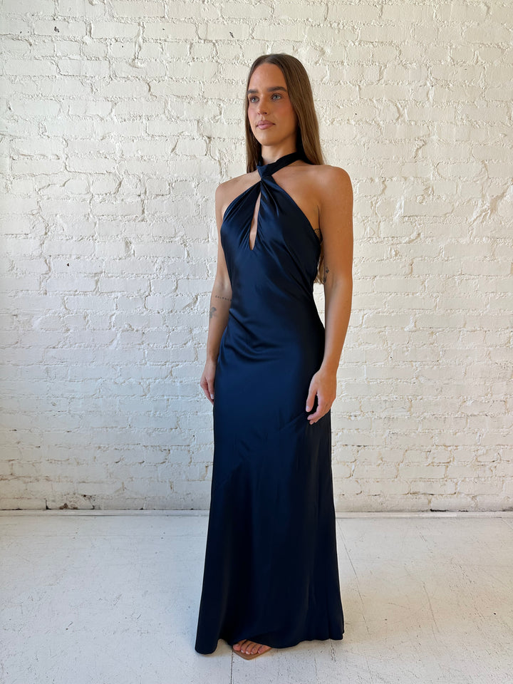 Woman wearing navy blue satin halter maxi dress with keyhole cutout, and open cowl back.