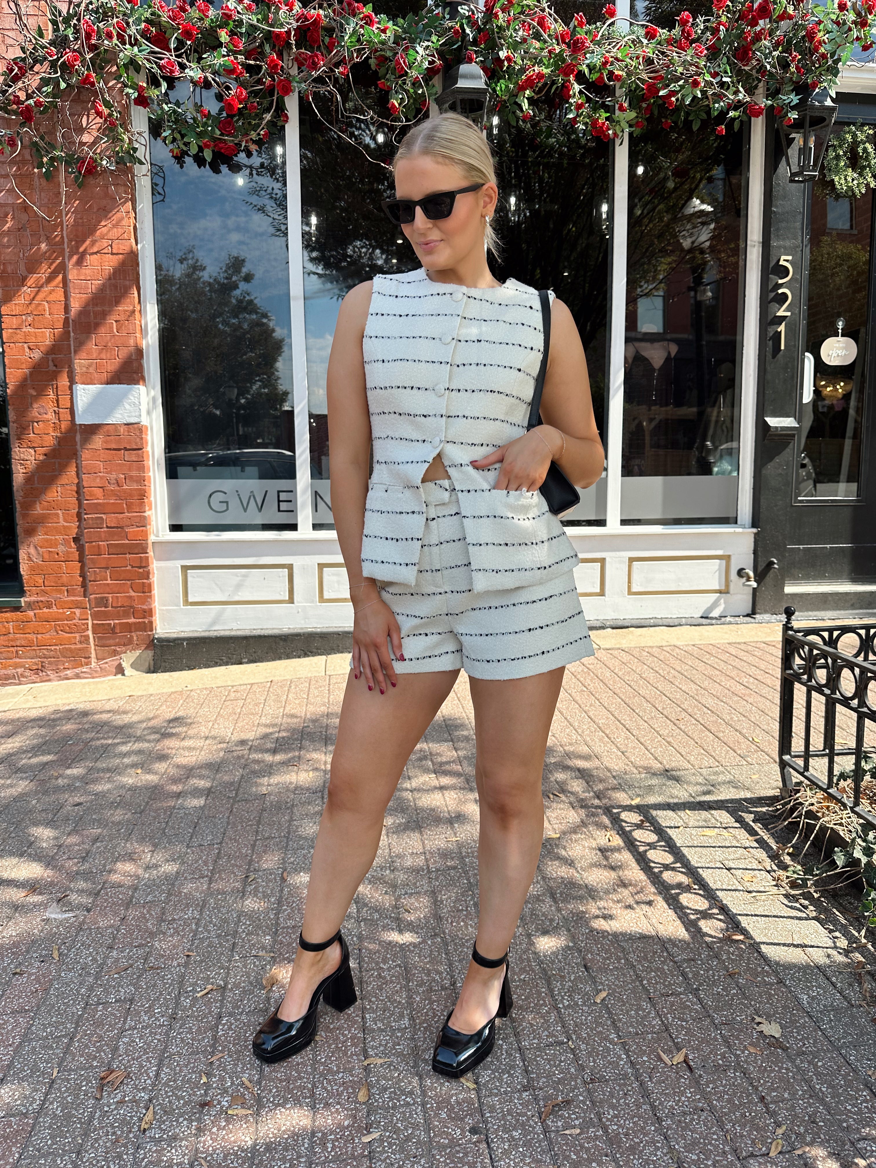 Woman wearing white and black striped tweed two piece set with high waisted short and button down top.