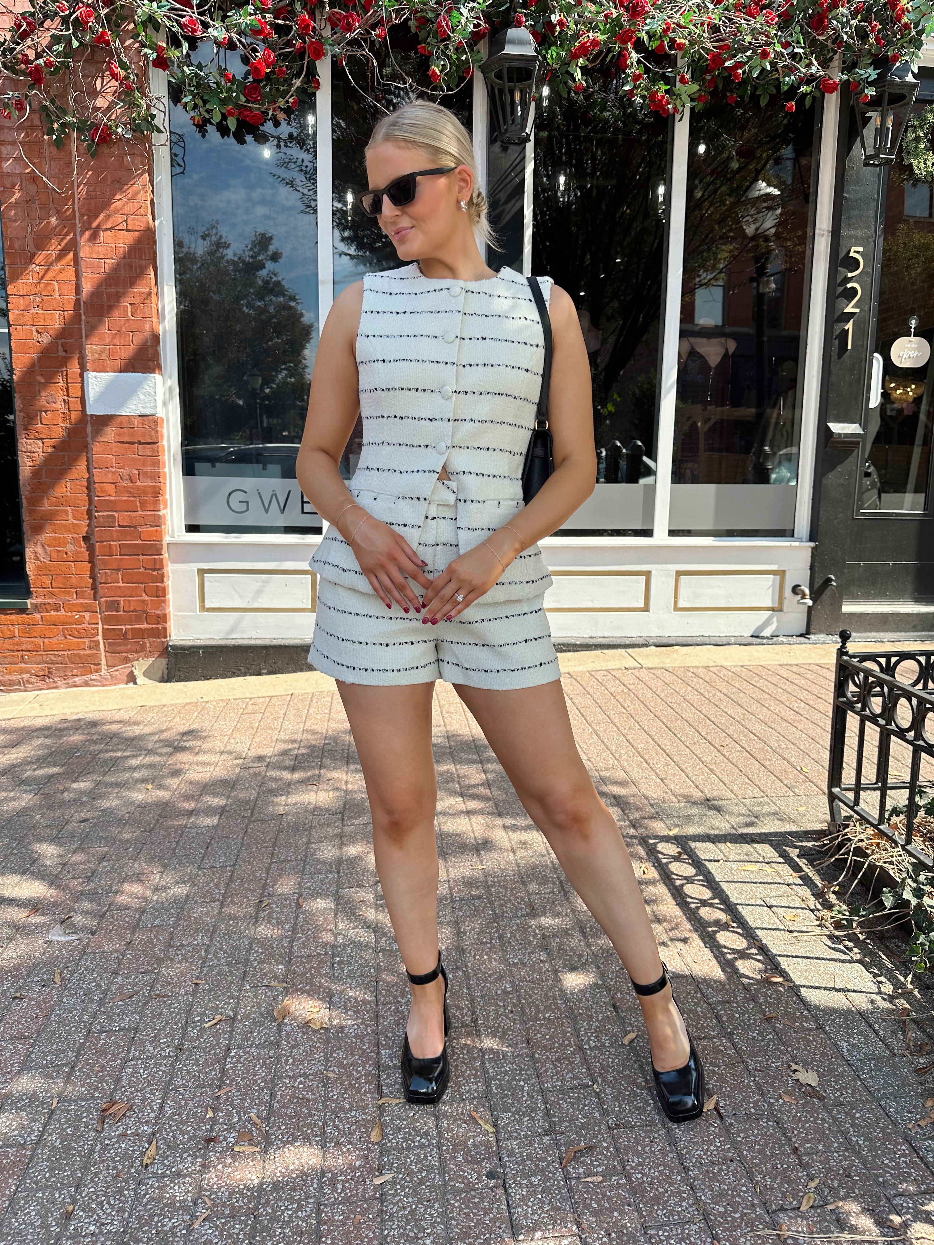 Woman wearing white and black striped tweed two piece set with high waisted short and button down top.