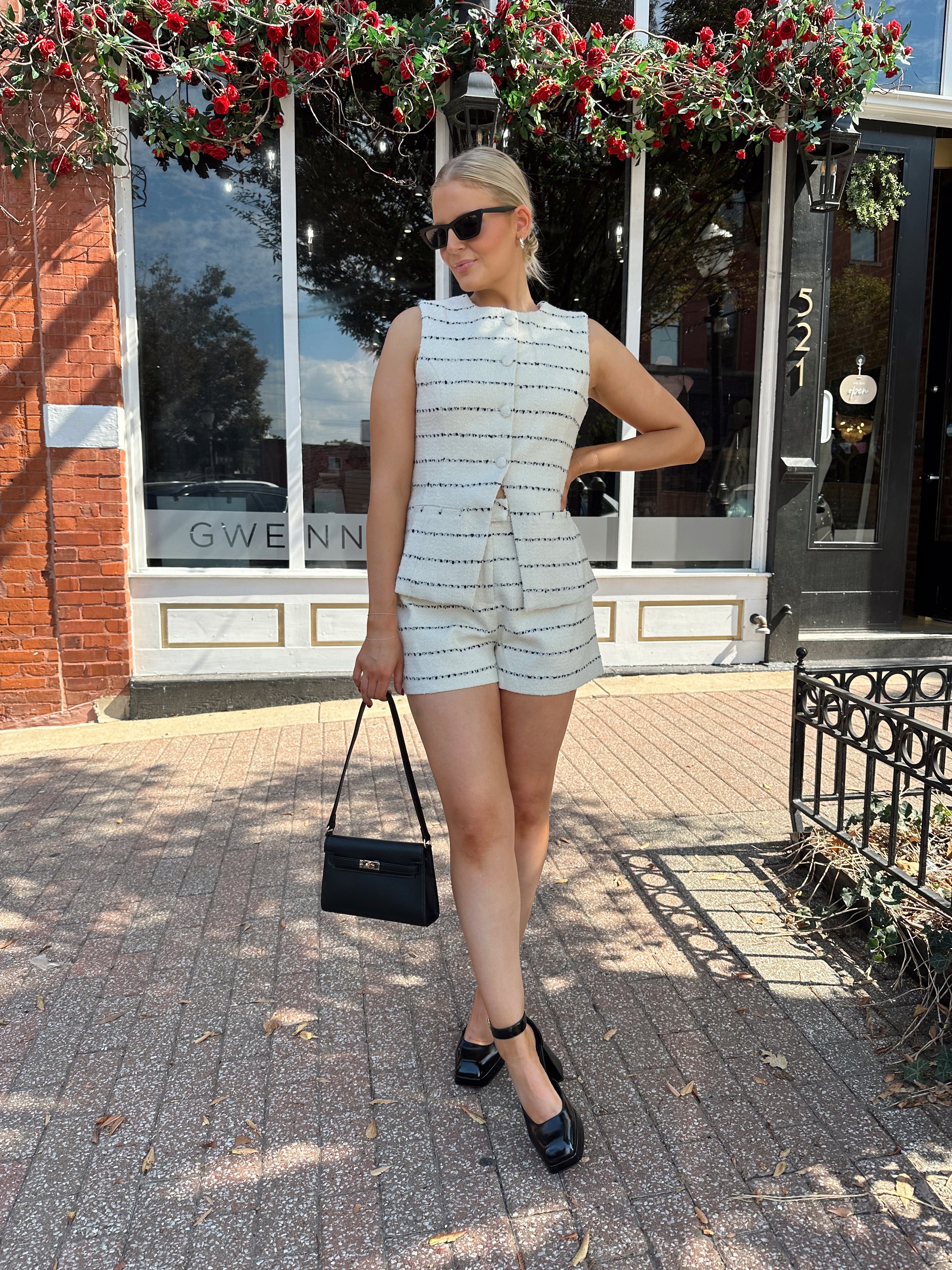 Woman wearing white and black striped tweed two piece set with high waisted short and button down top.