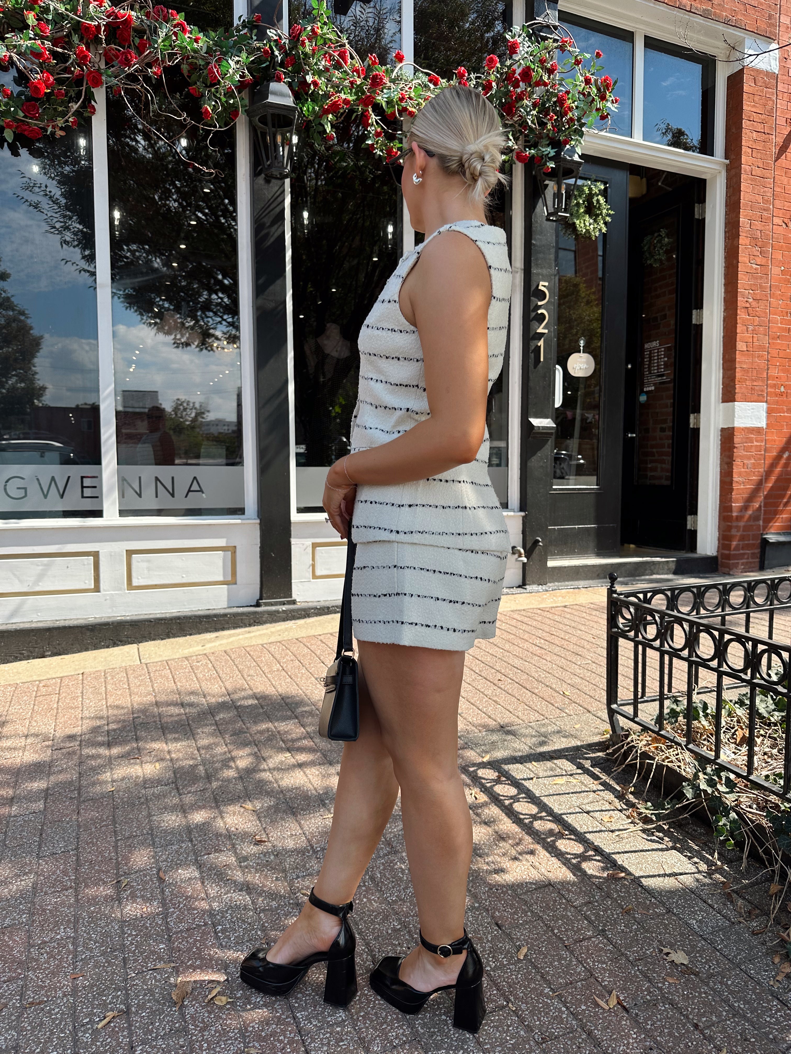 Woman wearing white and black striped tweed two piece set with high waisted short and button down top.