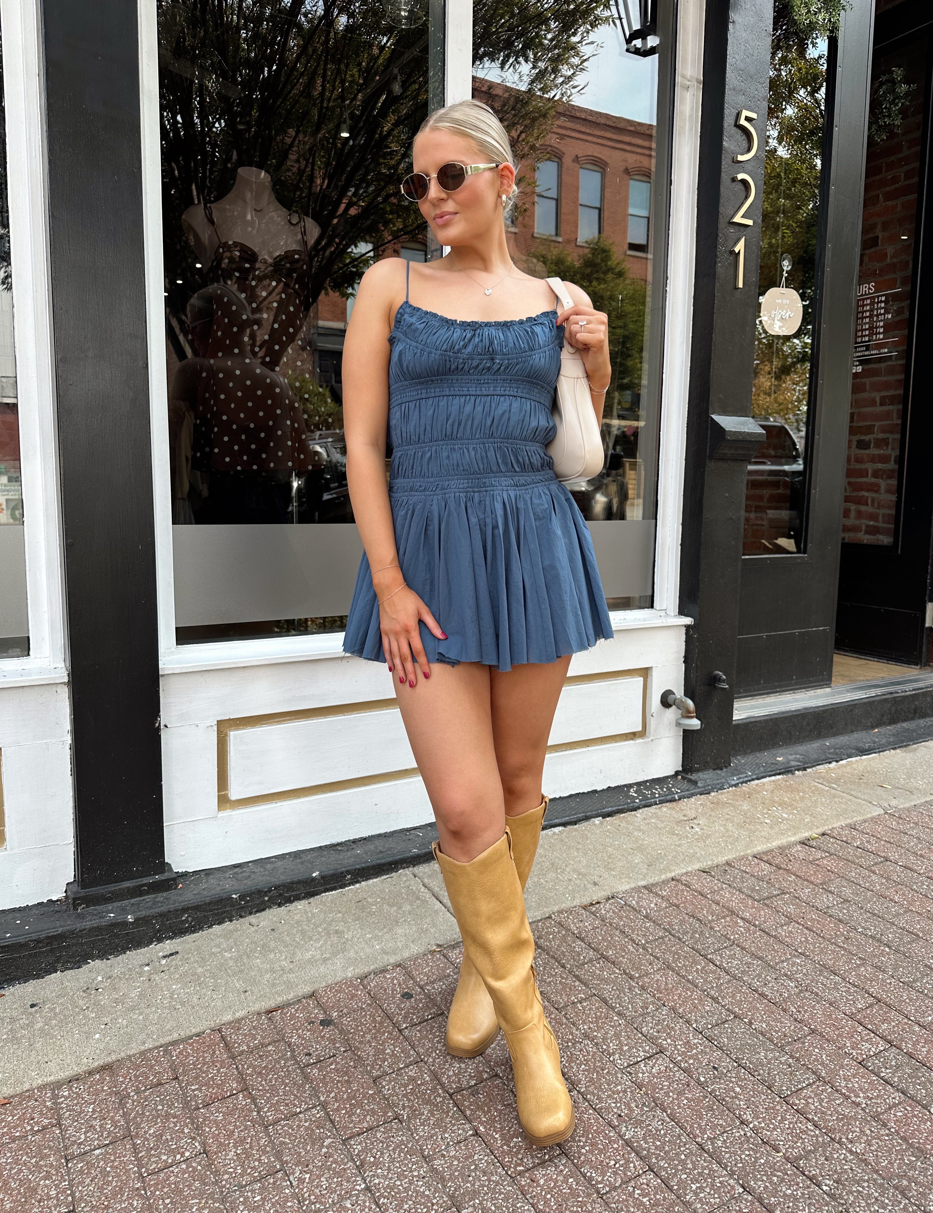 Woman wearing dusty blue smocked mini dress with built in shorts and adjustable straps.