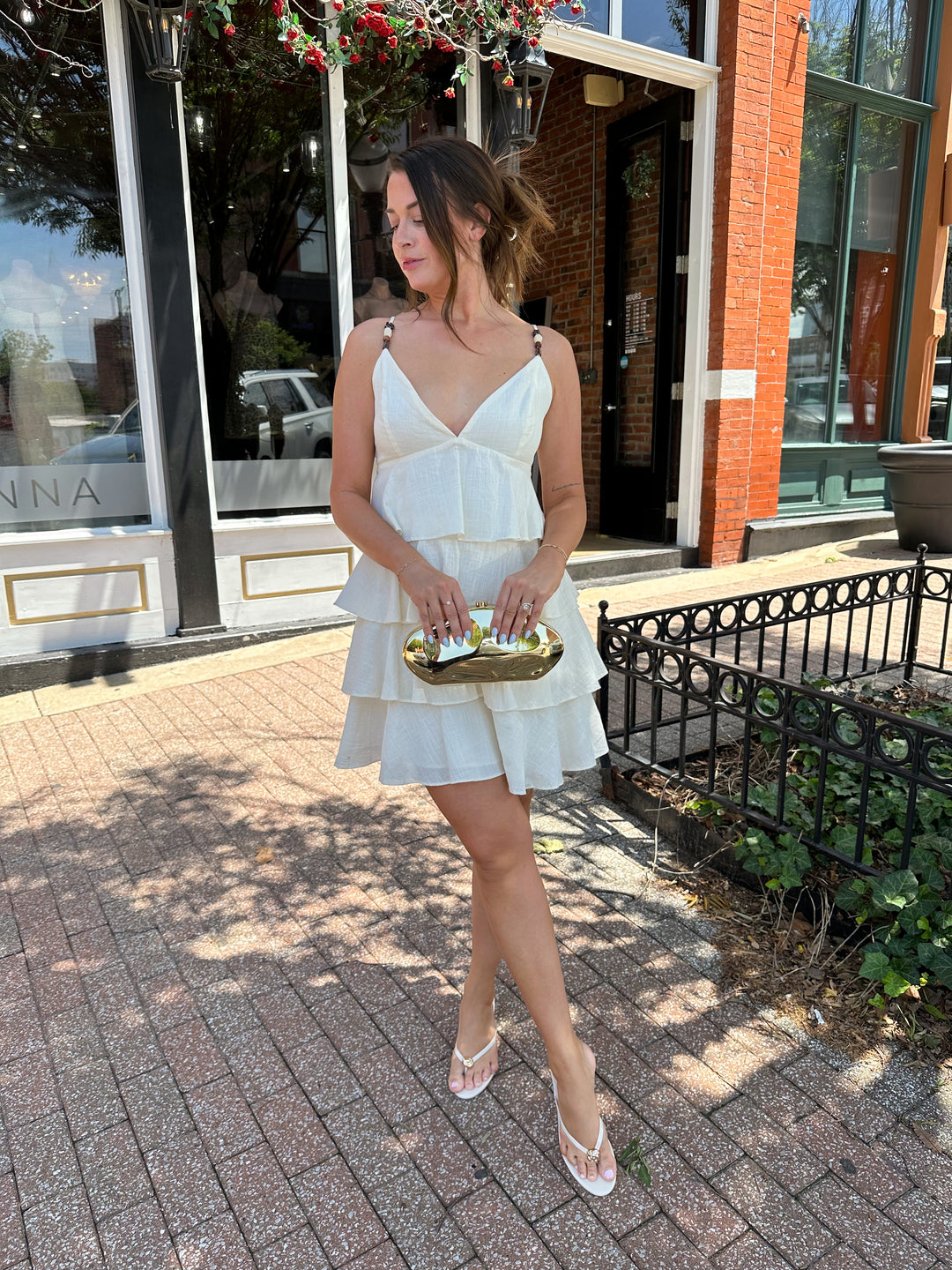 Woman wearing beige tiered mini dress with v-neckline, and beaded strap detailing. Has adjustable spaghetti straps.