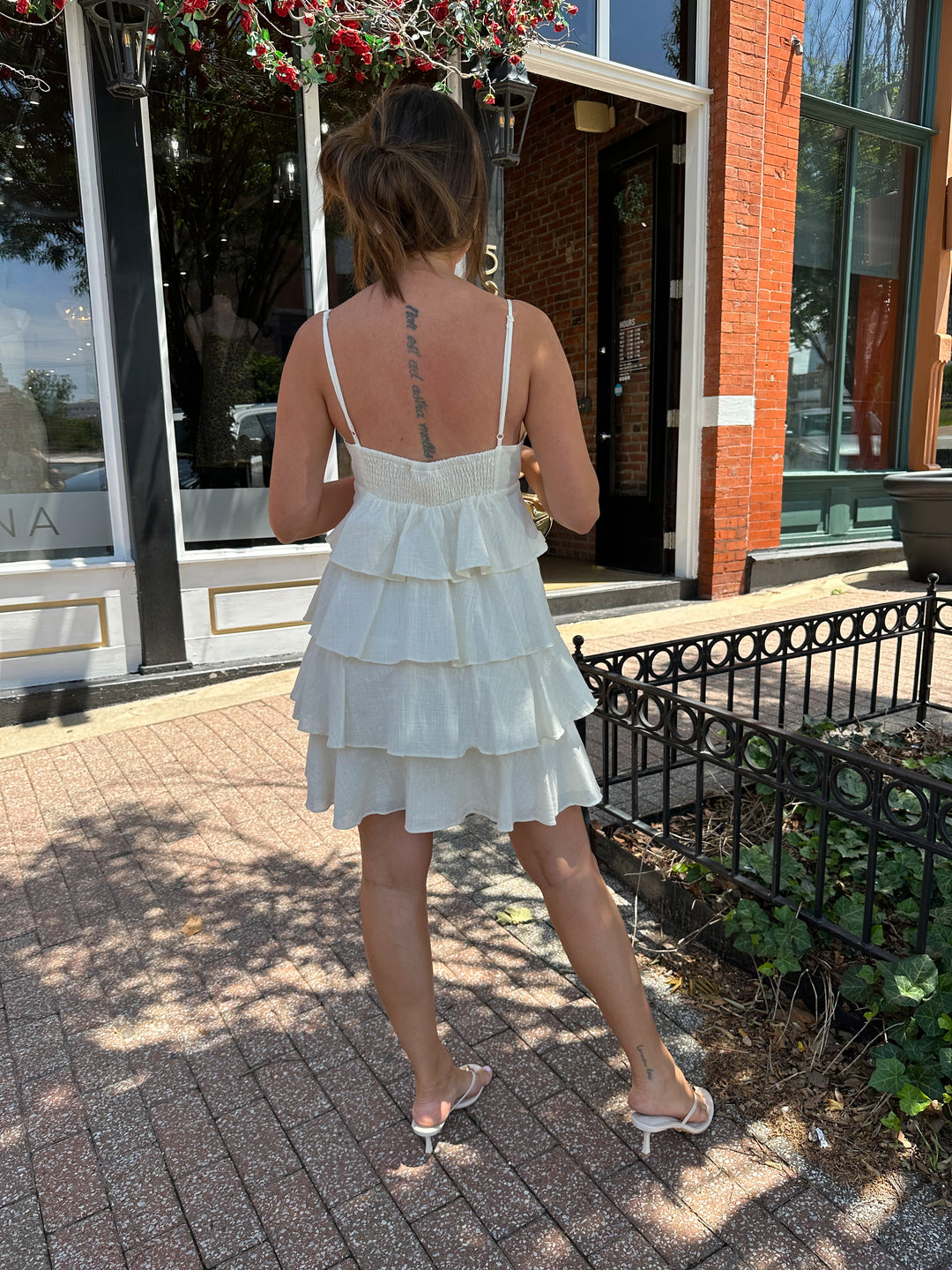 Woman wearing beige tiered mini dress with v-neckline, and beaded strap detailing. Has adjustable spaghetti straps.