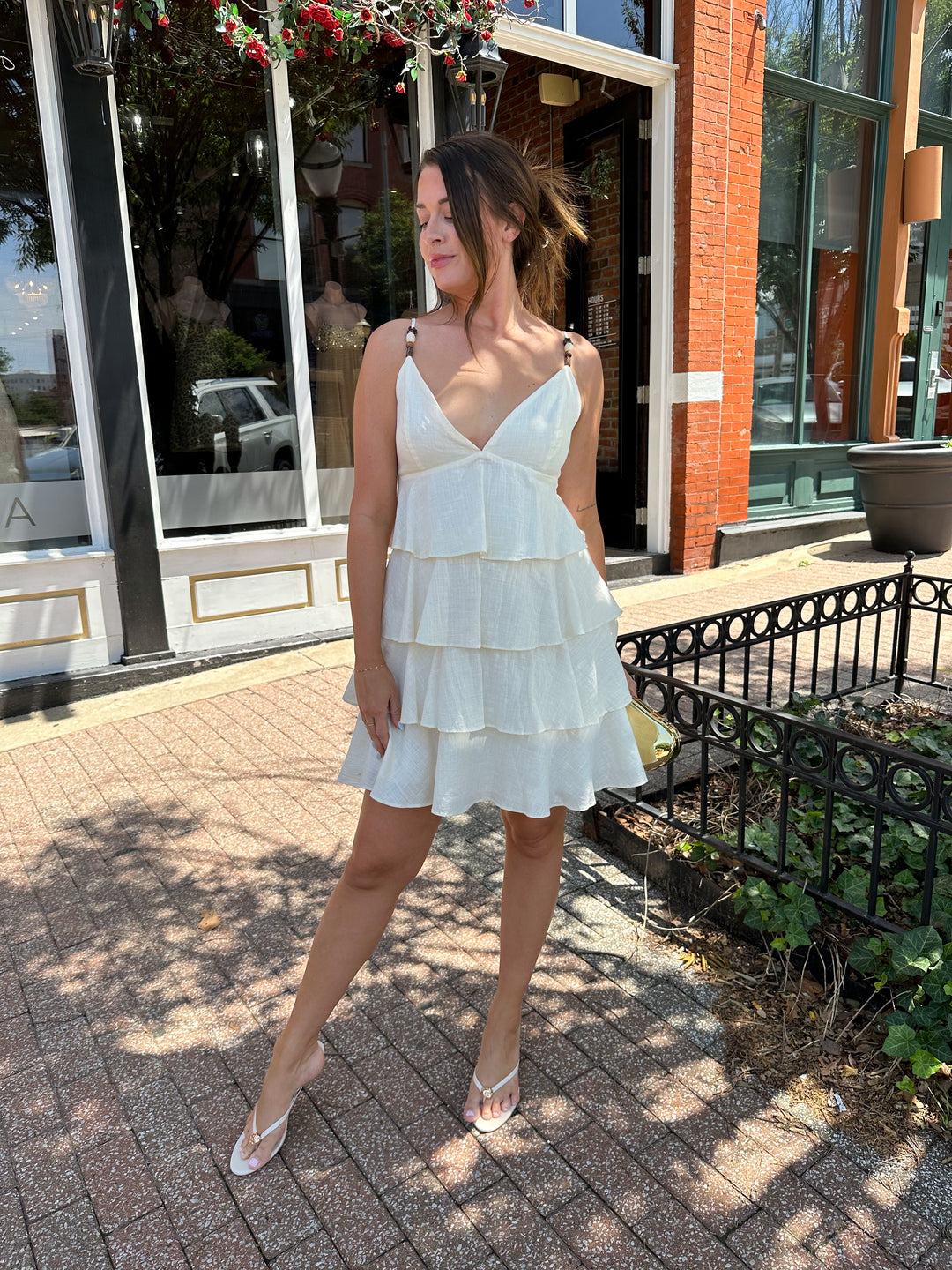 Woman wearing beige tiered mini dress with v-neckline, and beaded strap detailing. Has adjustable spaghetti straps.