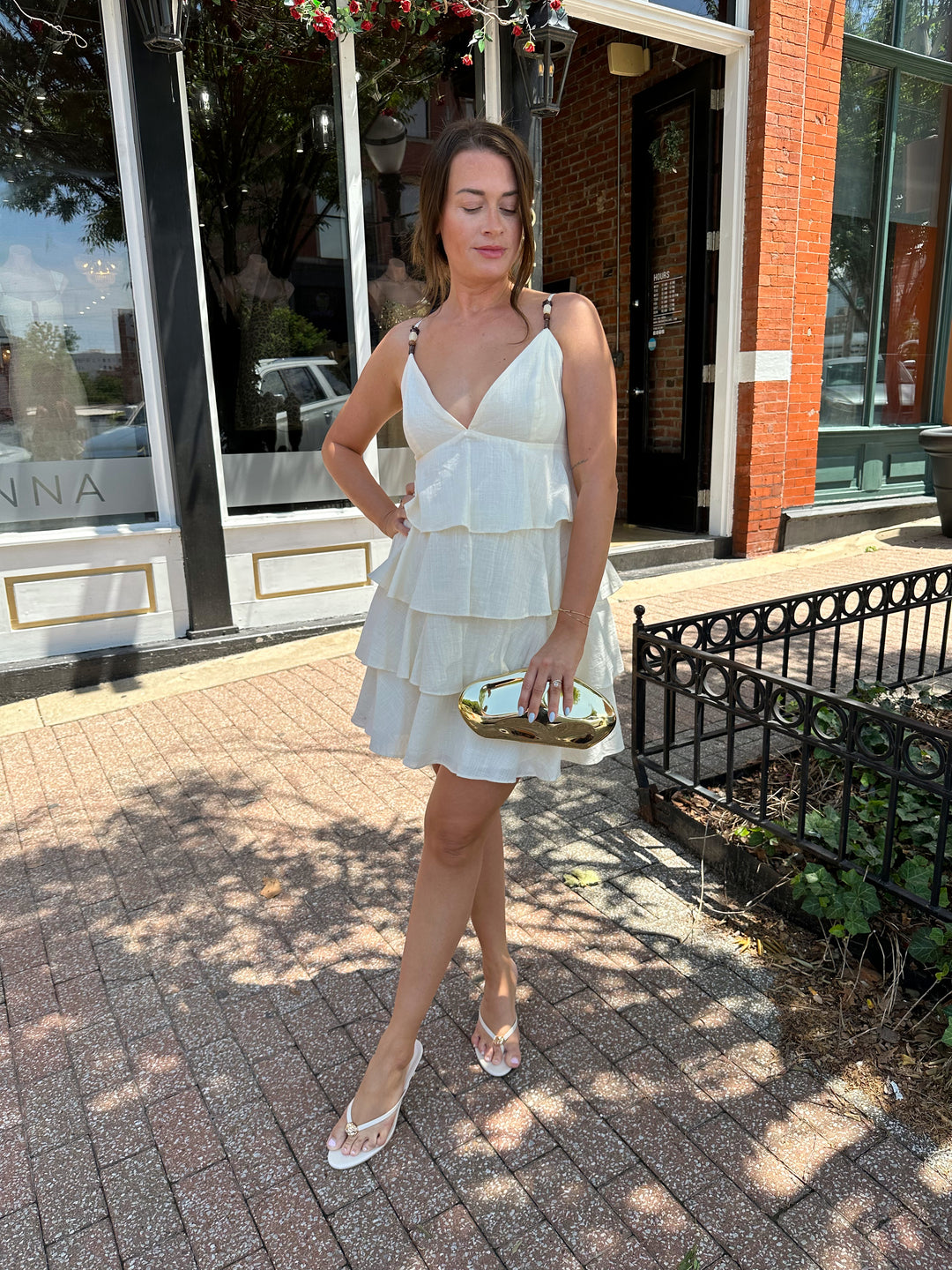 Woman wearing beige tiered mini dress with v-neckline, and beaded strap detailing. Has adjustable spaghetti straps.