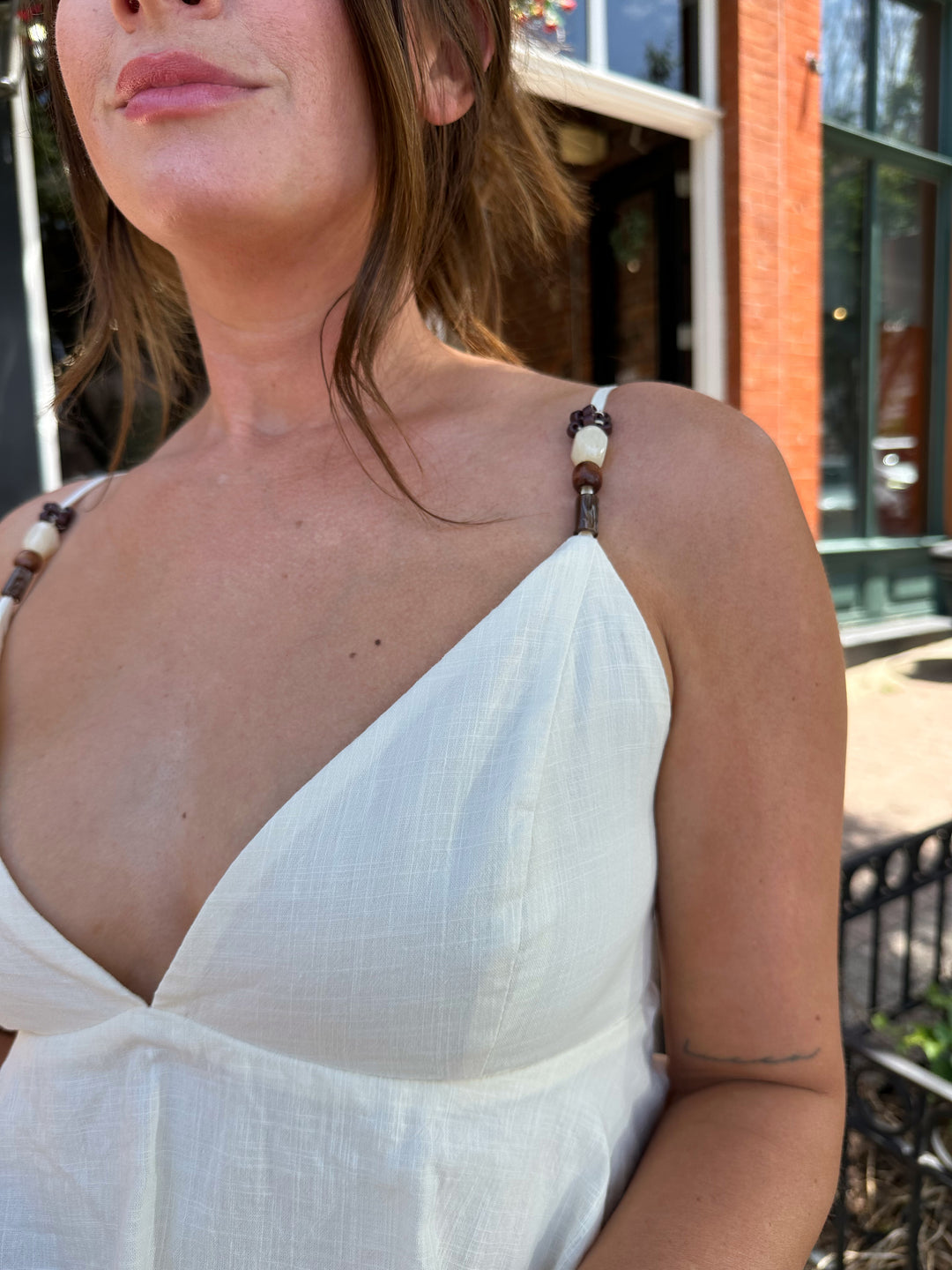 Woman wearing beige tiered mini dress with v-neckline, and beaded strap detailing. Has adjustable spaghetti straps.