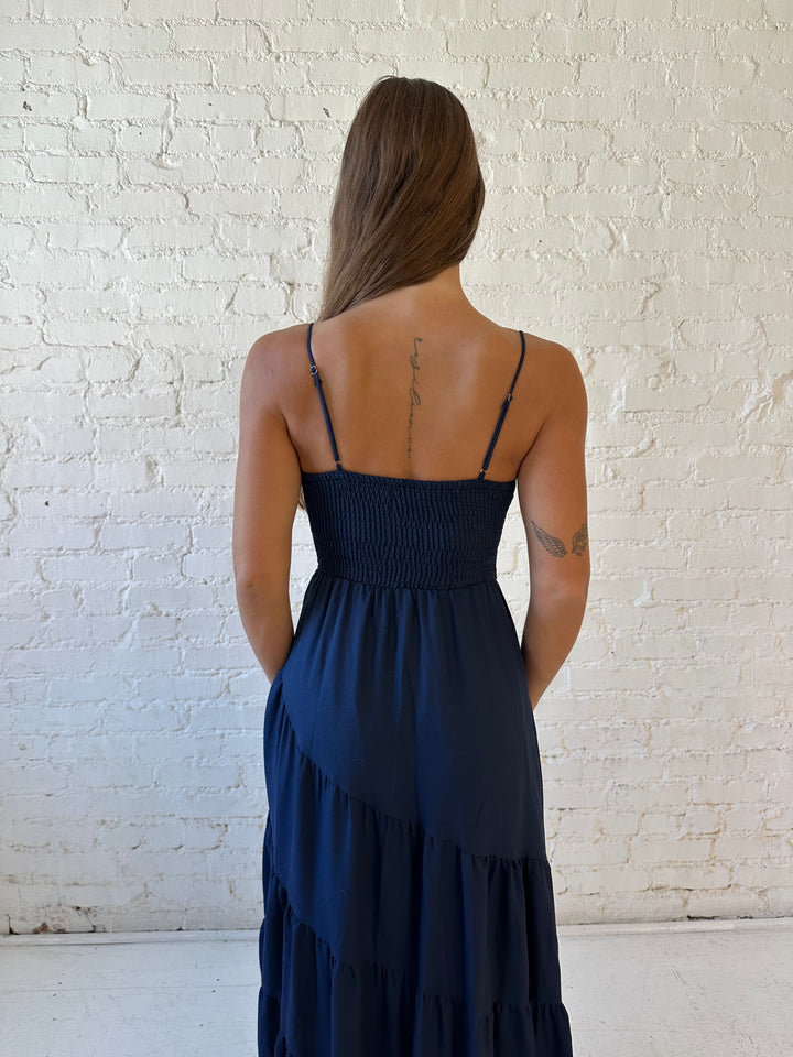 Woman wearing navy blue tiered maxi dress with twisted sweetheart neckline and smocked back.