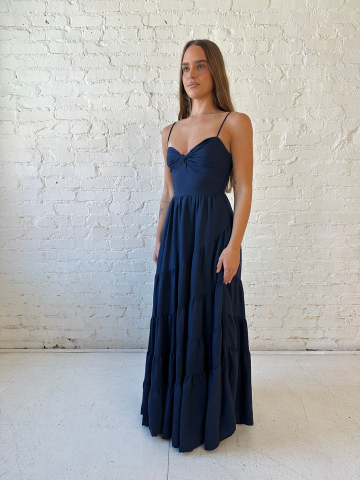 Woman wearing navy blue tiered maxi dress with twisted sweetheart neckline and smocked back.