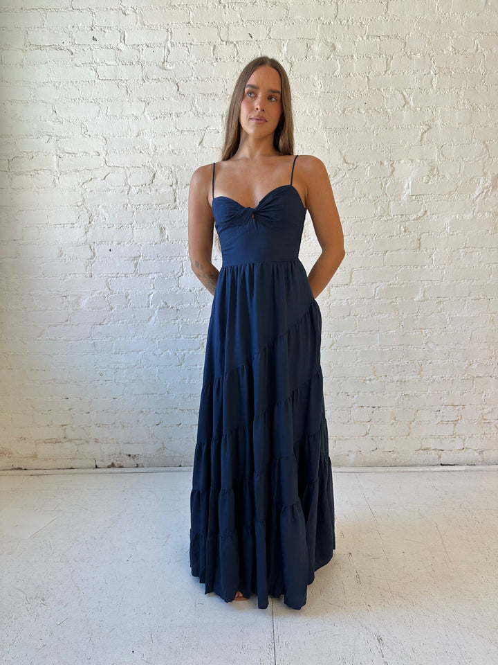 Woman wearing navy blue tiered maxi dress with twisted sweetheart neckline and smocked back.