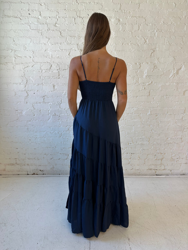 Woman wearing navy blue tiered maxi dress with twisted sweetheart neckline and smocked back.