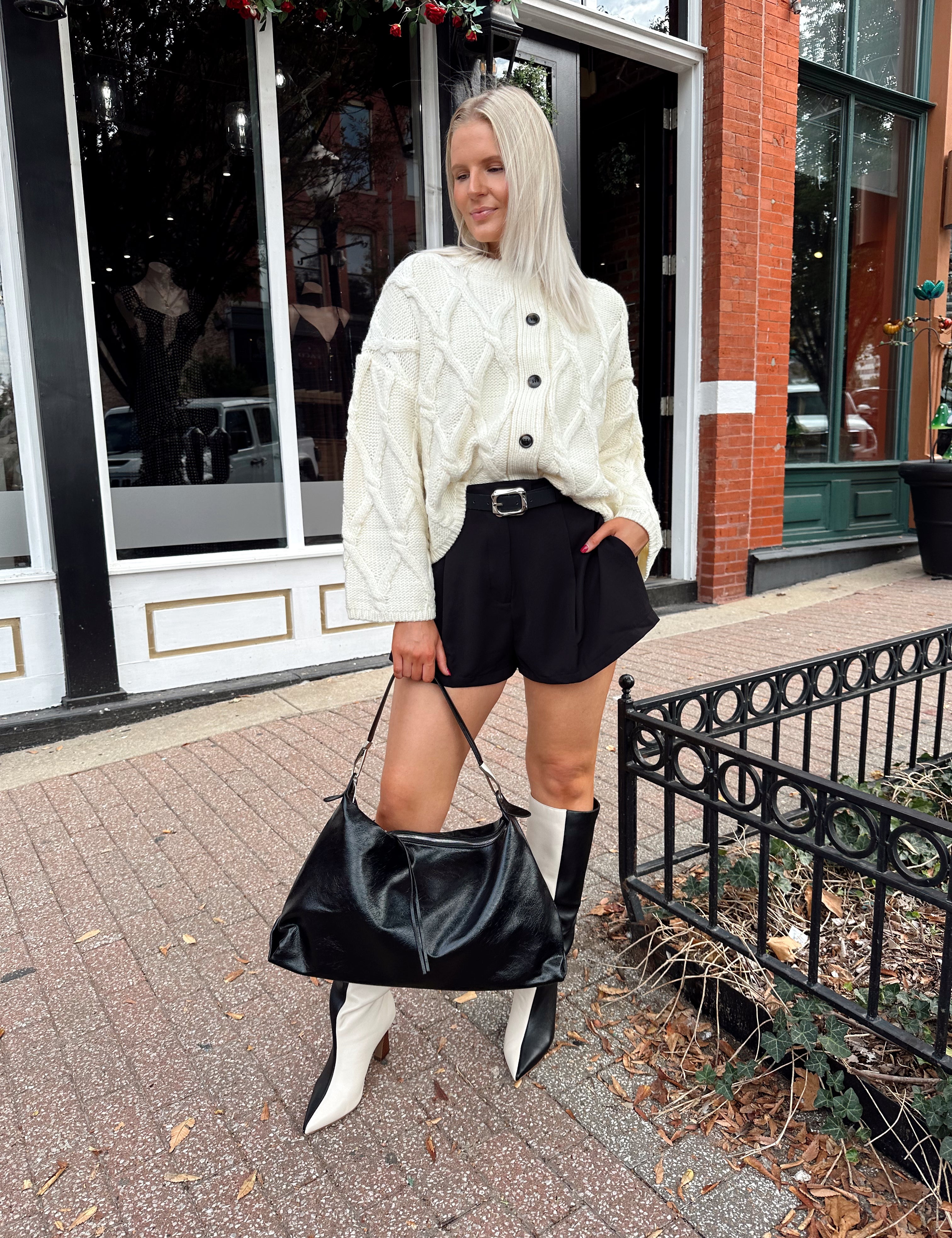 Woman wearing chunky off white button down cardigan with black shorts.