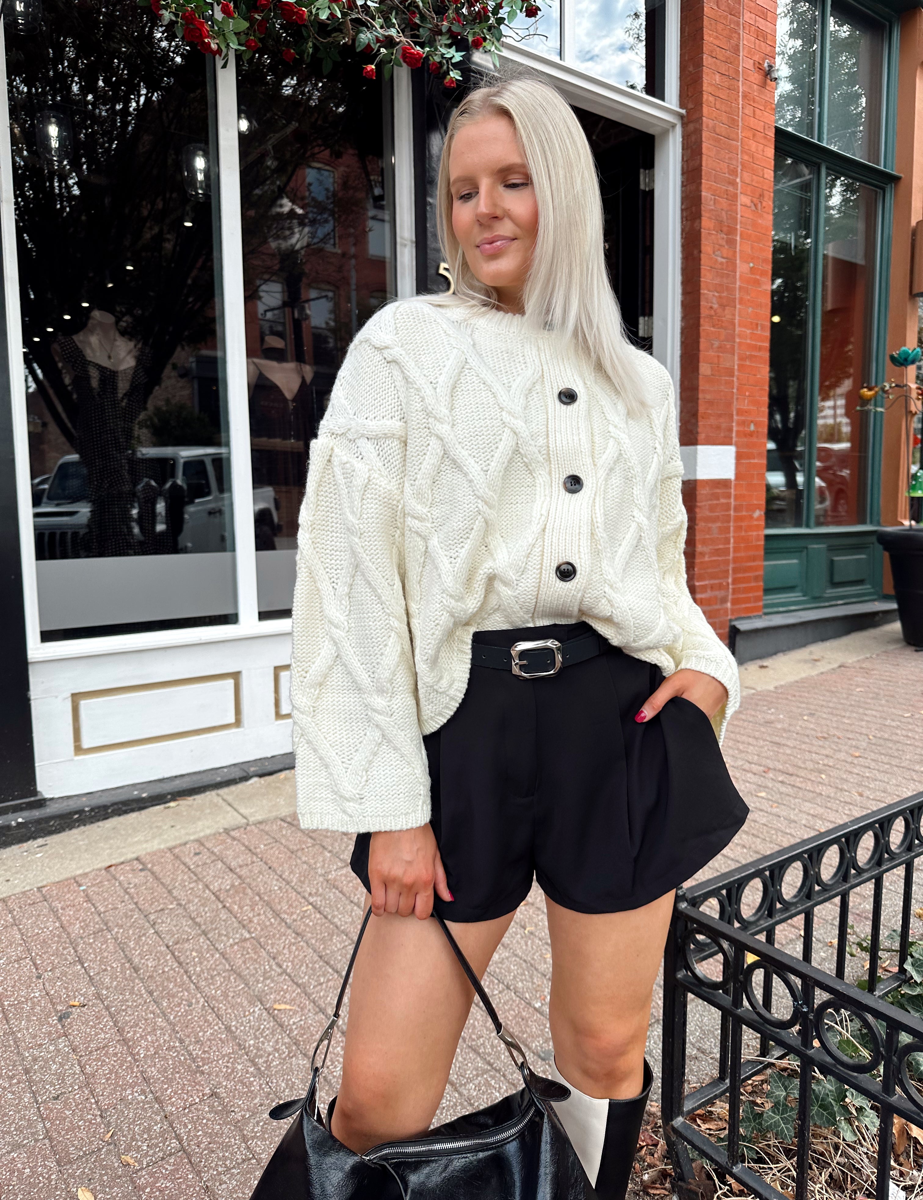 Woman wearing chunky off white button down cardigan with black shorts.