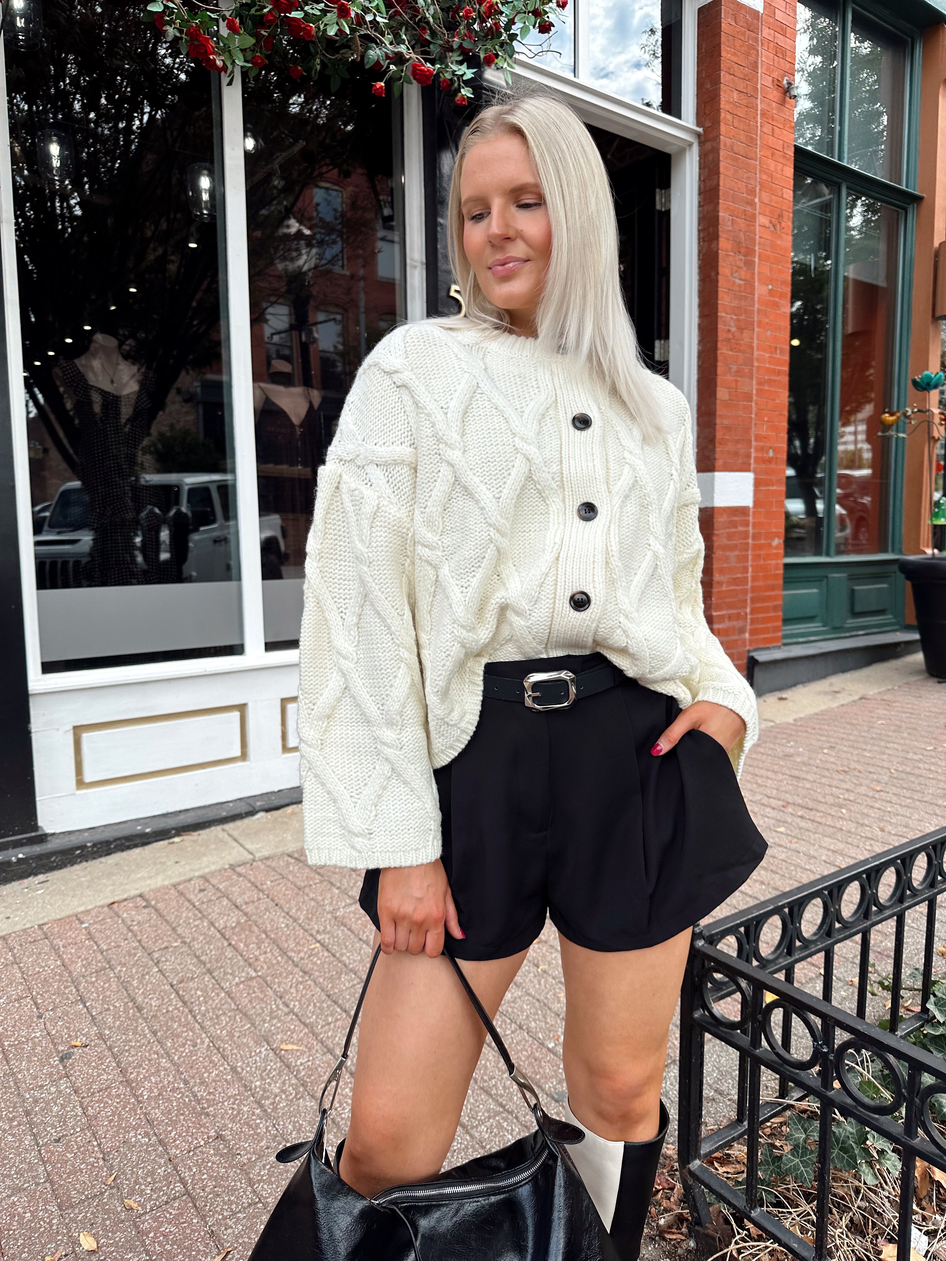 Woman wearing chunky off white button down cardigan with black shorts.