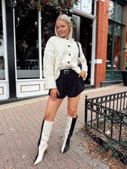 Woman wearing chunky off white button down cardigan with black shorts.