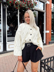 Woman wearing chunky off white button down cardigan with black shorts.