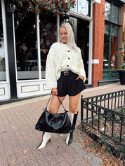 Woman wearing chunky off white button down cardigan with black shorts.