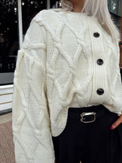 Woman wearing chunky off white button down cardigan with black shorts.