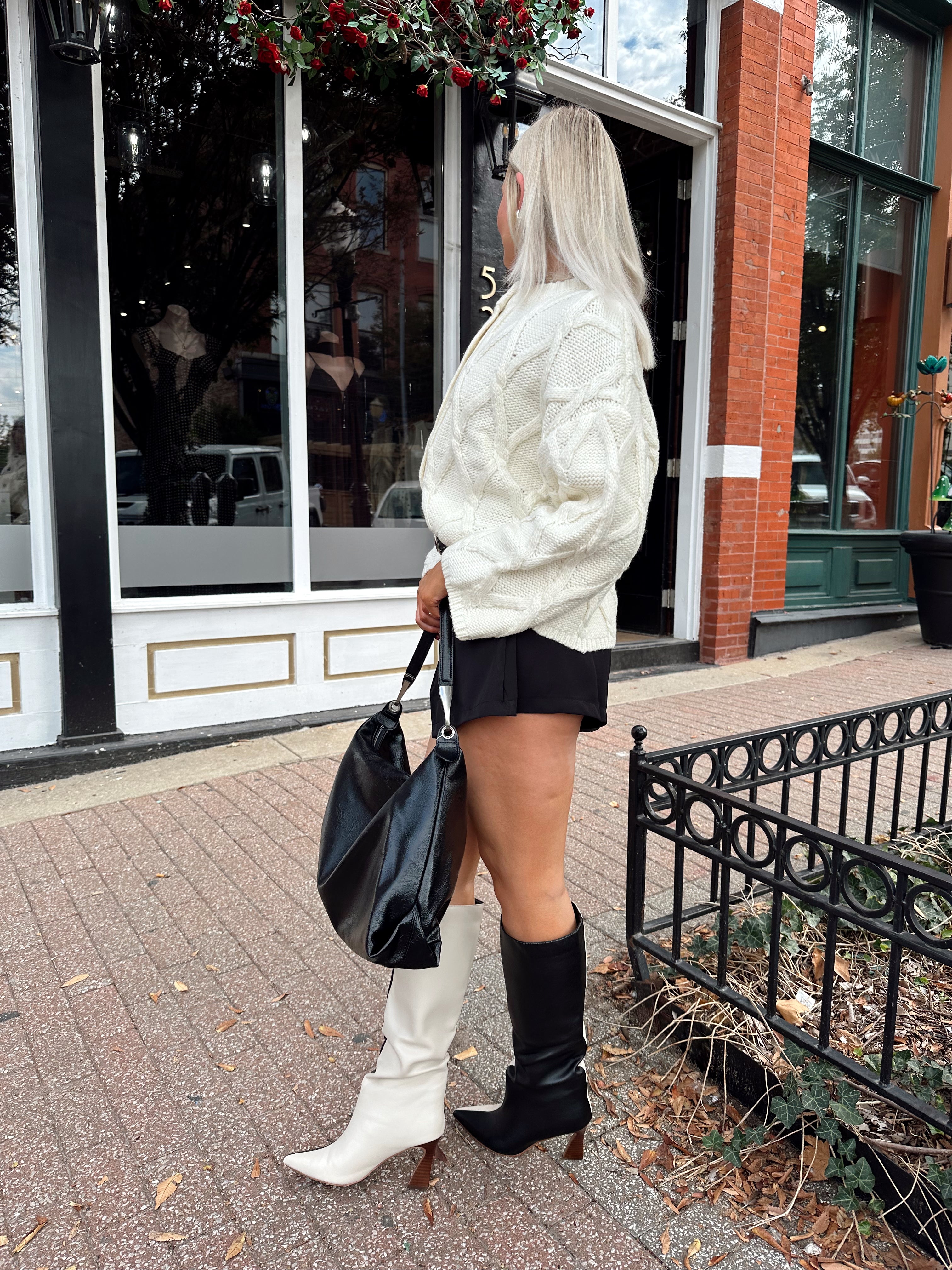 Woman wearing chunky off white button down cardigan with black shorts.