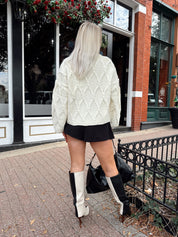 Woman wearing chunky off white button down cardigan with black shorts.
