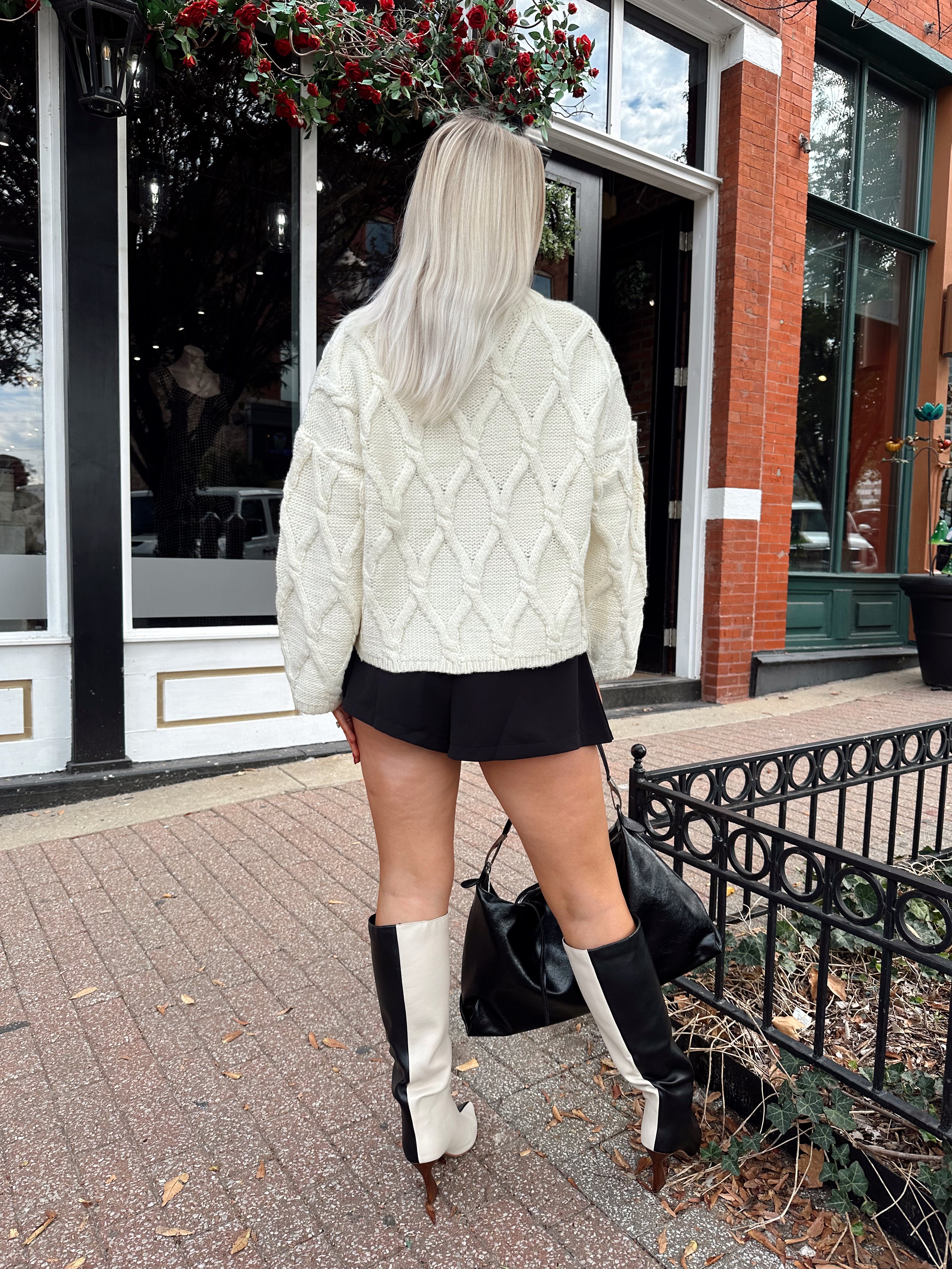 Woman wearing chunky off white button down cardigan with black shorts.