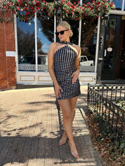 Woman wearing black and white polka dot satin mini dress with halter scarf neckline. 